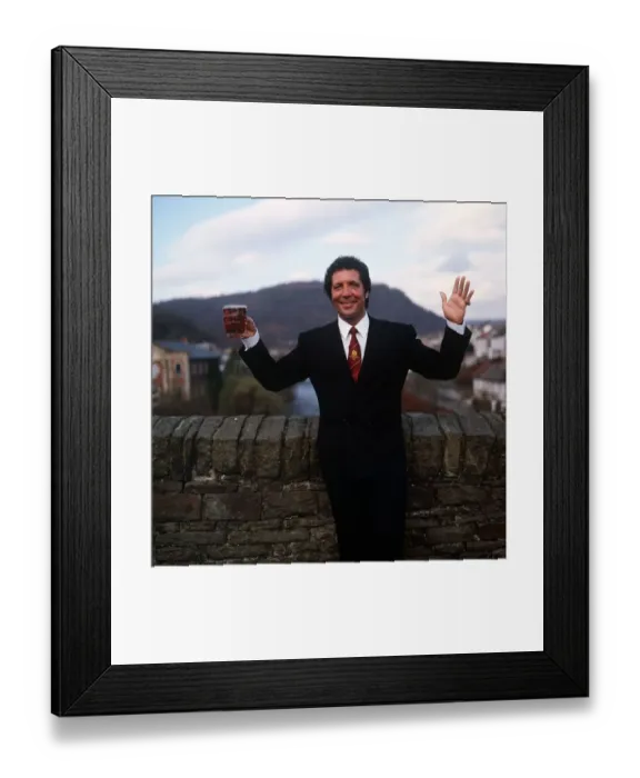 Framed Print : Tom Jones Singer in his home town in Wales standing by brick wall holding pint glass of