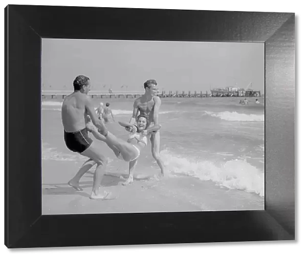 Two men throwing a young woman into the sea on Bournemouth beach. 10th Aust 1952