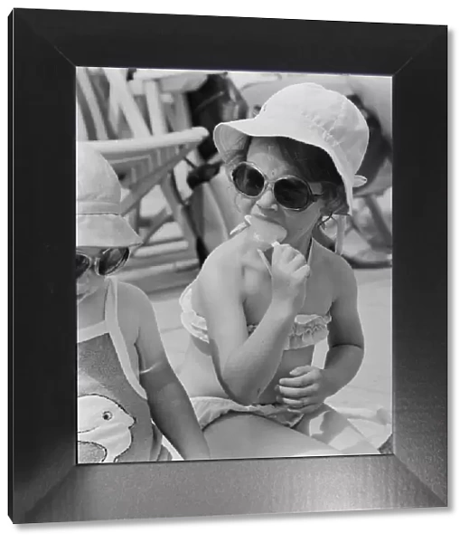 A young girl sitting on the beach, enjoying an ice lolly. 26th June 1979