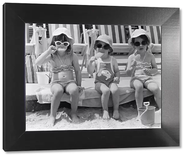 Three young girls sitting on the beach, enjoying an ice lolly. 26th June 1979