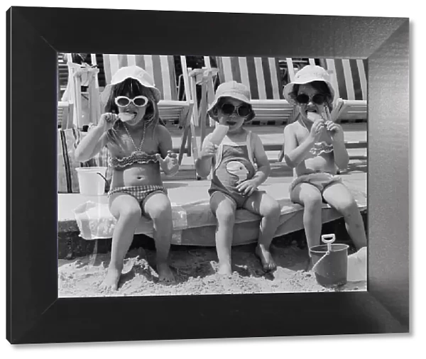 Three young girls sitting on the beach, enjoying an ice lolly. 26th June 1979