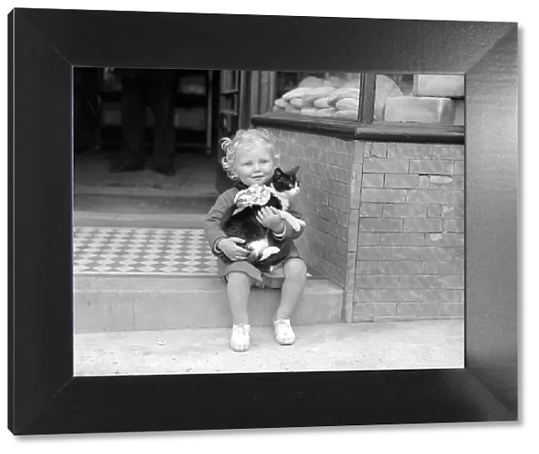 Little Girl With Cat A small child sitting on the steps of a shop holding a cat in