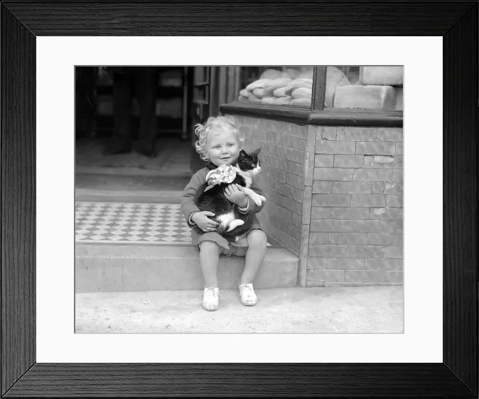 Framed Print : Little Girl With Cat A small child sitting on the steps of a shop holding a cat in Framed Print : Little Girl With Cat A small child sitting on the steps of a shop holding a cat in