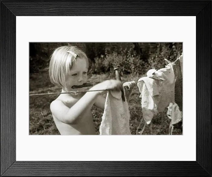 Framed Print : A young girl hanging out the washing to dry at Hampstead day Nursery in London Framed Print : A young girl hanging out the washing to dry at Hampstead day Nursery in London