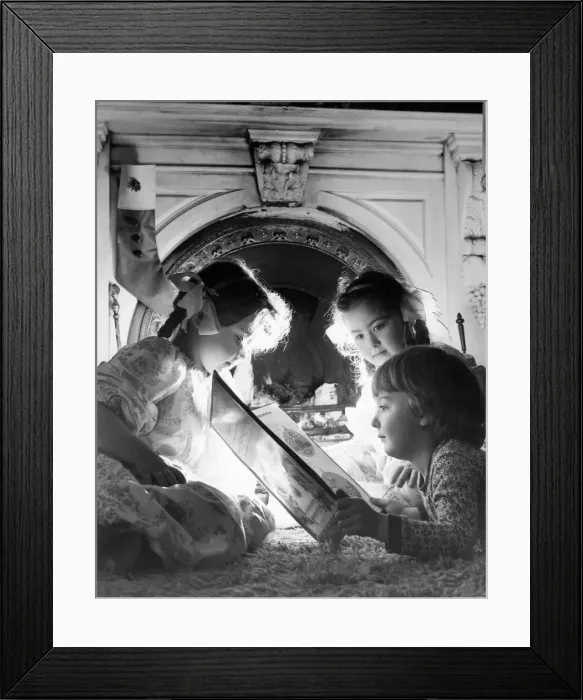 Framed Print : Three children listen to a fairytale in front of roaring fire at Christmas time