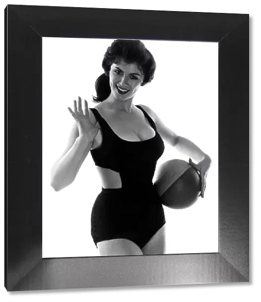 Fashion July 1958 Model from 1950s wearing a black swimsuit holding ball