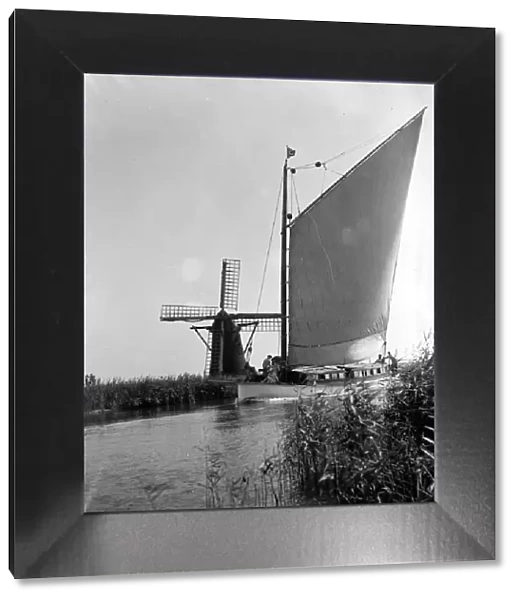 A traditional Norfolk Broad yachts sailing past one of the many windmill water pumps that