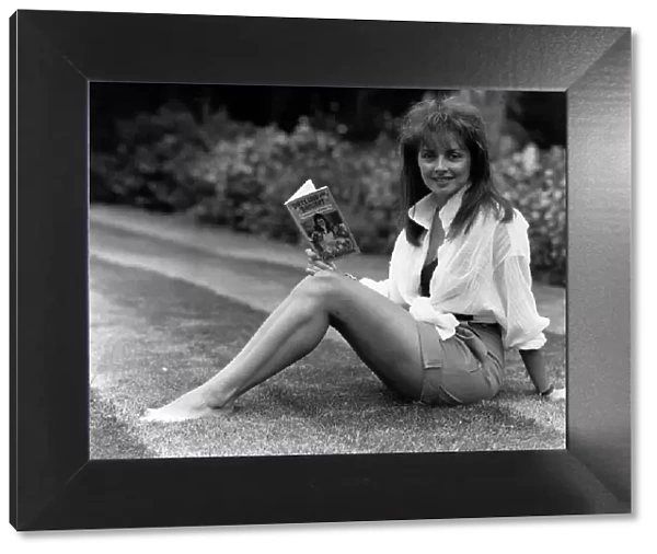 Carol Vorderman TV Presenter sitting on grass lawn holding paperback book
