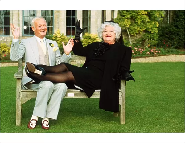 John Inman Comedy Actor and Mollie Sugden Comedy Actress sitting on wooden bench seat in