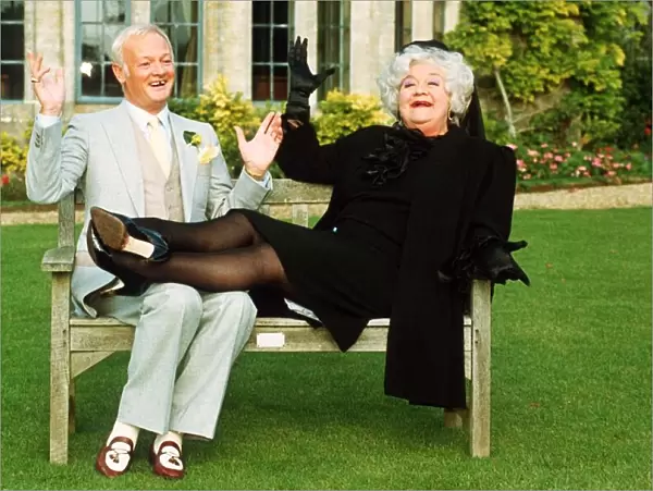 John Inman Comedy Actor and Mollie Sugden Comedy Actress sitting on wooden bench seat in