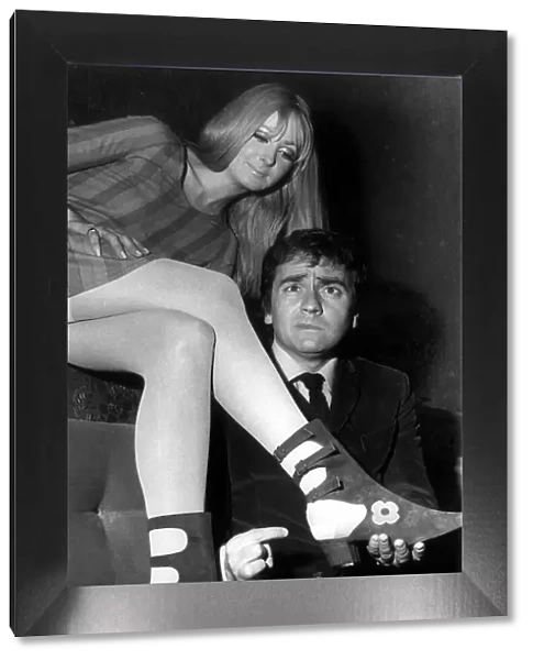 Comedian Dudley Moore pulling a face inspects a pair of boots called 'Sex Puss'