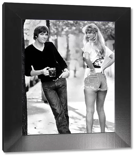 Actor Steve Alder holding a pint of beer as he poses with a model wearing denim hot pants