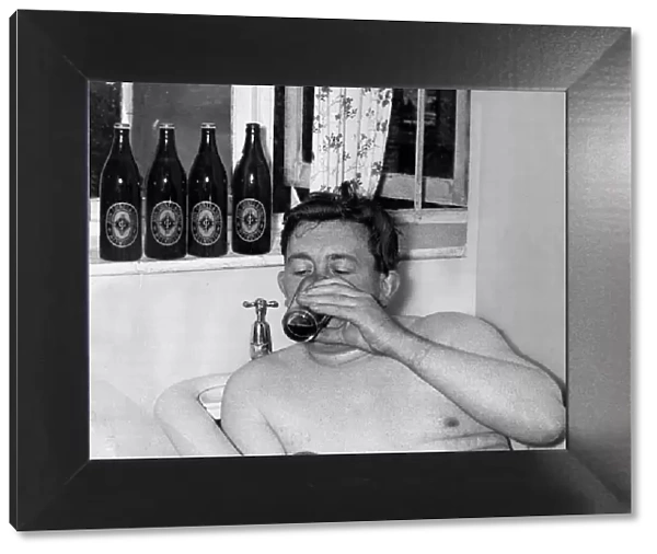 A man relaxes in the bath drinking a bottle of beer September 1955
