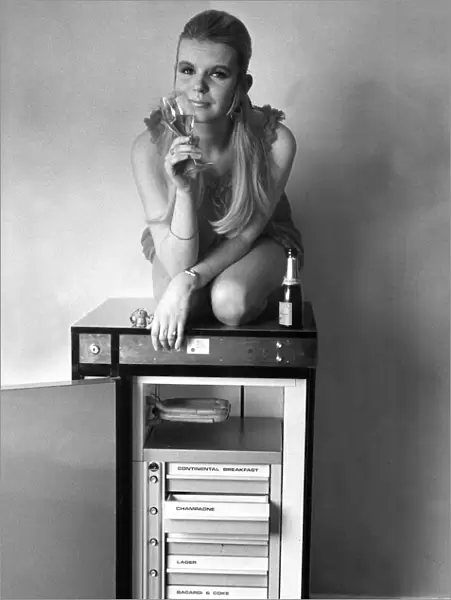 A women sits on top of a fridge with a bottle of chilled champagne holding a glass
