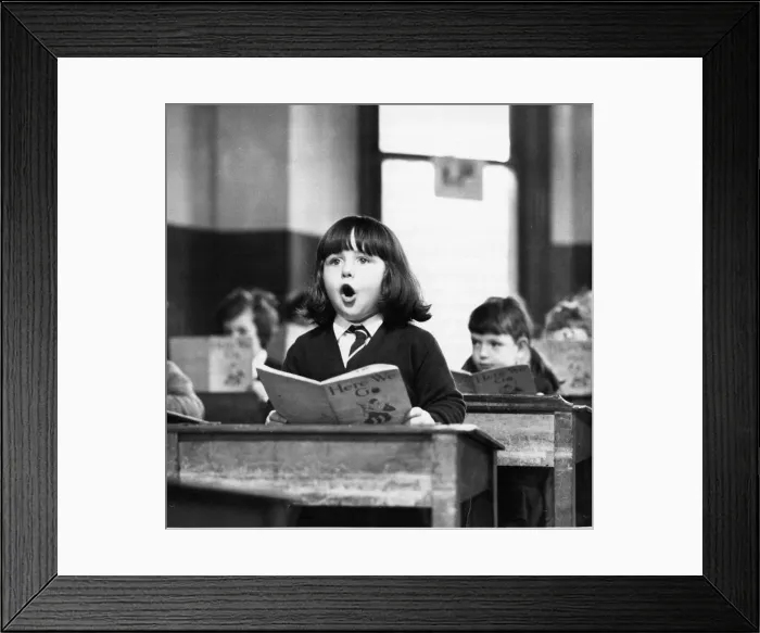 Framed Print : A young girl reads her Here We Go book aloud in class Framed Print : A young girl reads her Here We Go book aloud in class