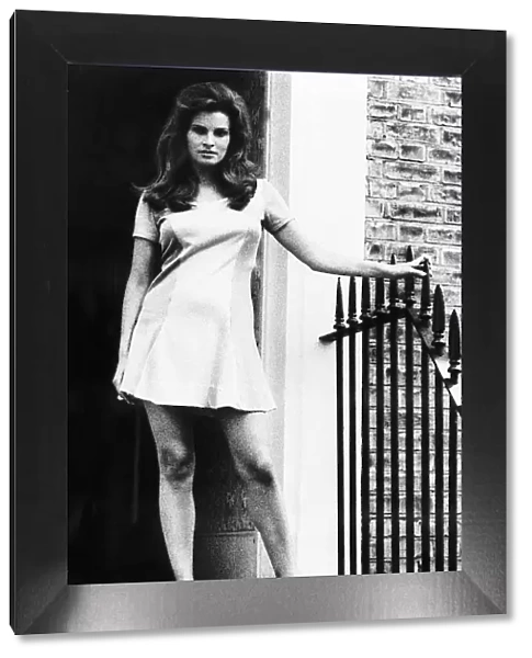 Raquel Welch standing by door in small dress holding onto the side December