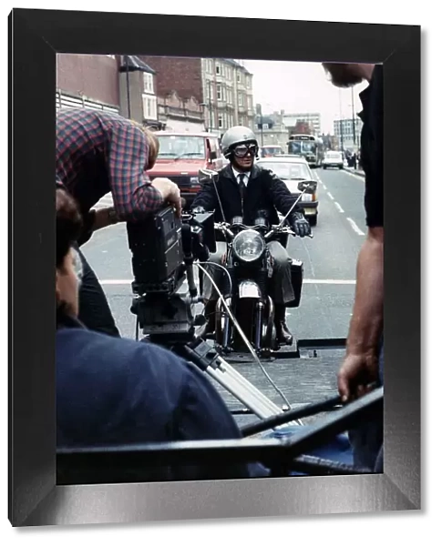 Michael Elphick actor sitting on motor bike attached rig on the back of lorry filming for