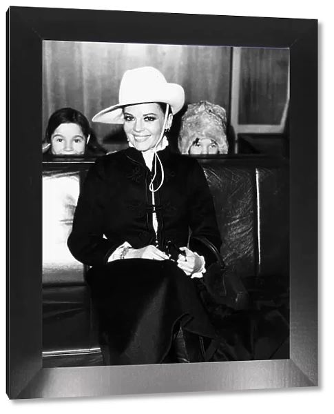 Natalie Wood waits for her flight at London airport peeping pver the seats are her