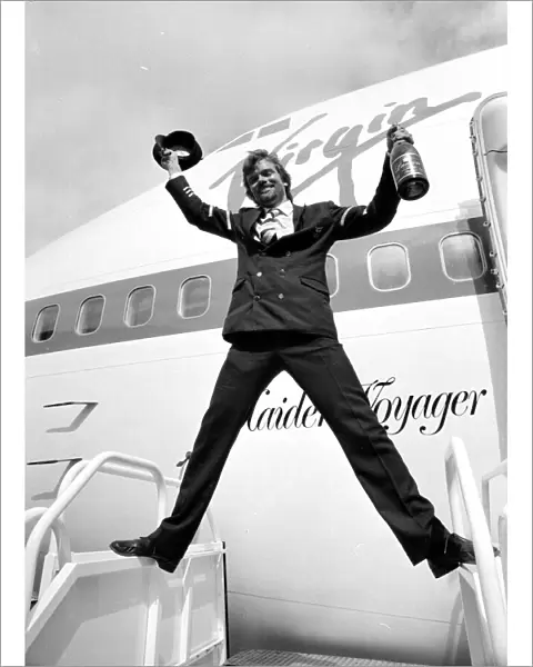 Richard Branson holding a bottle of champagne and pilots hat as he celebrates Virgin