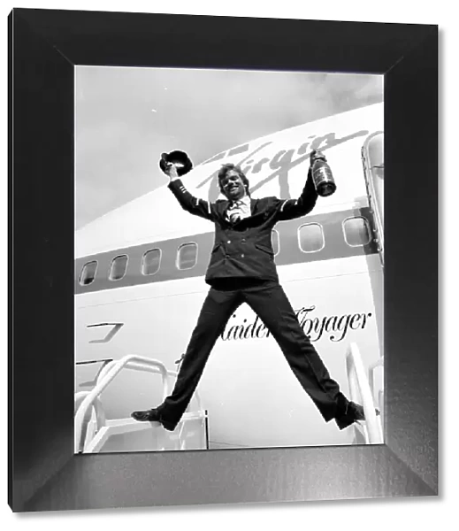Richard Branson holding a bottle of champagne and pilots hat as he celebrates Virgin