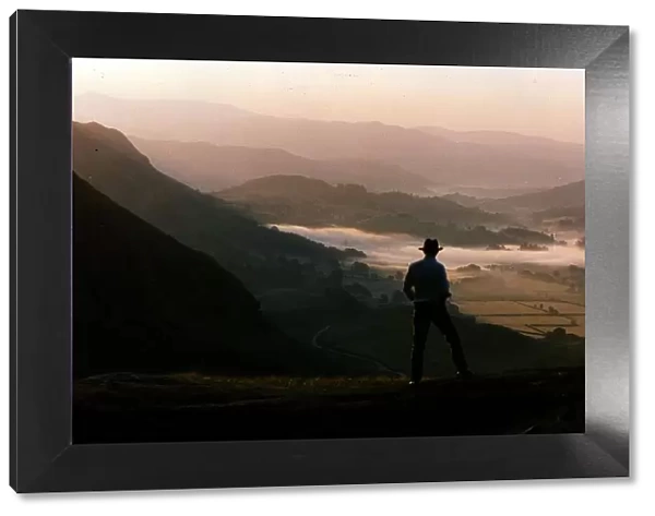 Dawn rises over the Lake District as a walker travels along a lakeland pass
