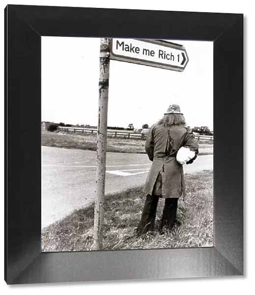 man stands below a road sign 'Make me Rich'