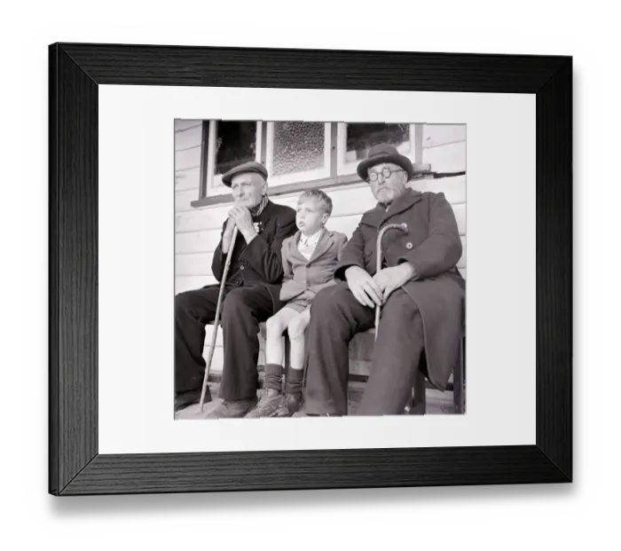 Framed Print : A young boy sits down with two old men on a bench. circa 1940
