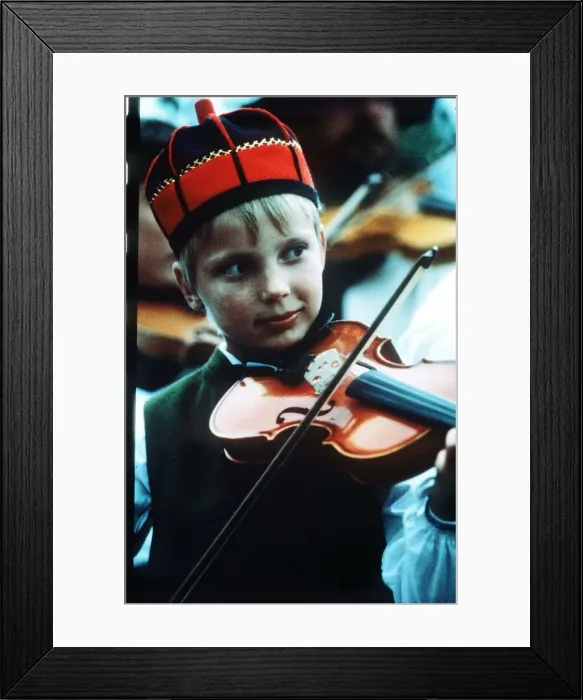 Framed Print : Sweden boy playing violin wearing red and blue traditional hat circa 1990