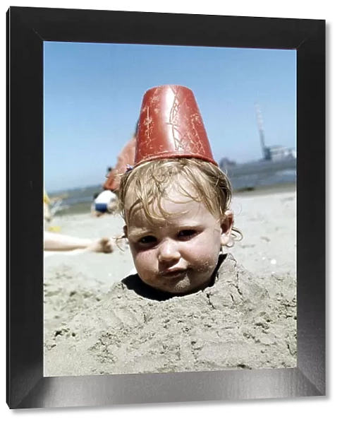 Summer holidays July 1976 - Boy buried in sand with red plastic Bucket on his head