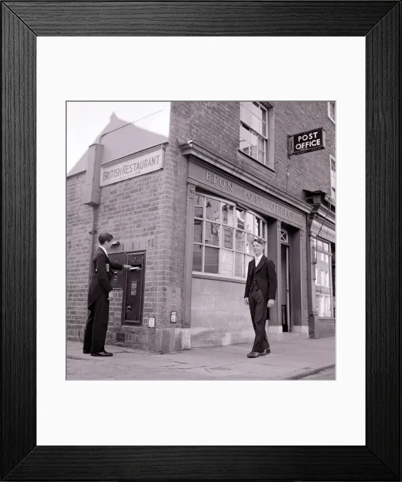 Framed Print : Eton schoolboy walks past Eton Post Office whilst another boy posts a letter dressed in