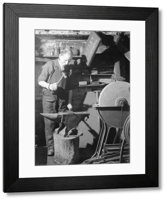 Framed Print : A Blacksmith works in his forge, hammering out a metal sheet on his anvil. Circa 1940 Framed Print : A Blacksmith works in his forge, hammering out a metal sheet on his anvil. Circa 1940