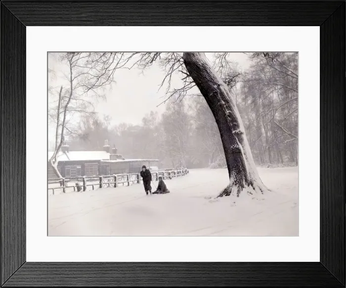 Framed Print : Boys playing the snow near their home. One child pulls his friend along on a home made Framed Print : Boys playing the snow near their home. One child pulls his friend along on a home made