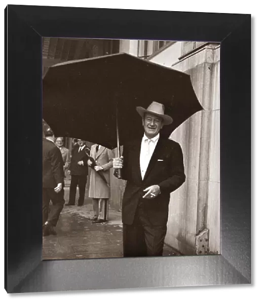 John Wayne standing under a big black umbrella in the rain in London October 1960