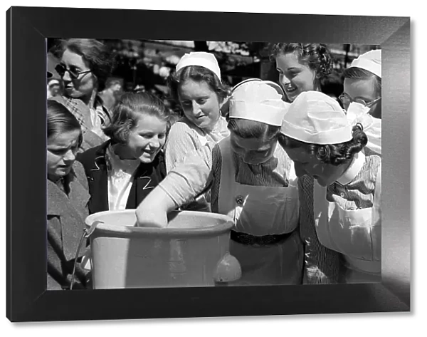 Nurses dunk their hands into a bucket at Barts Fair circa 1938