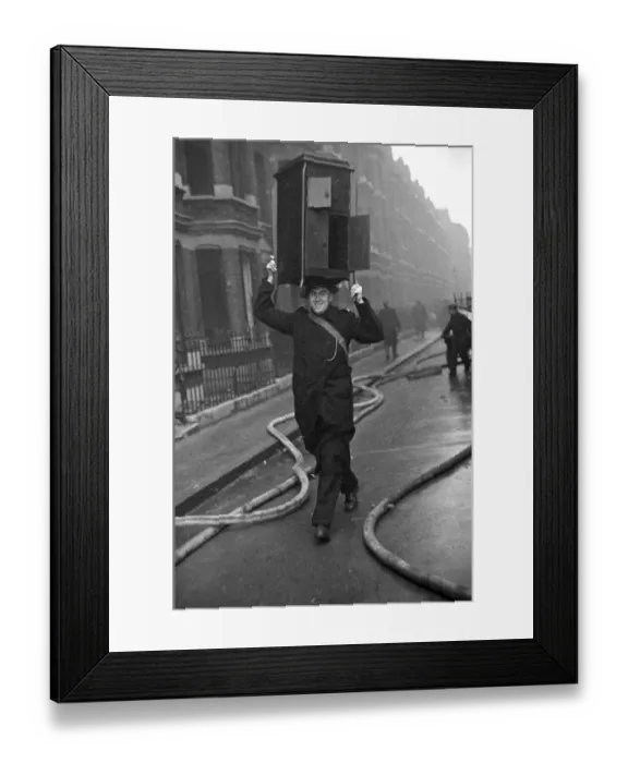 Framed Print : A cheery policeman with a cabinet balance on his head helps salvage furniture following a