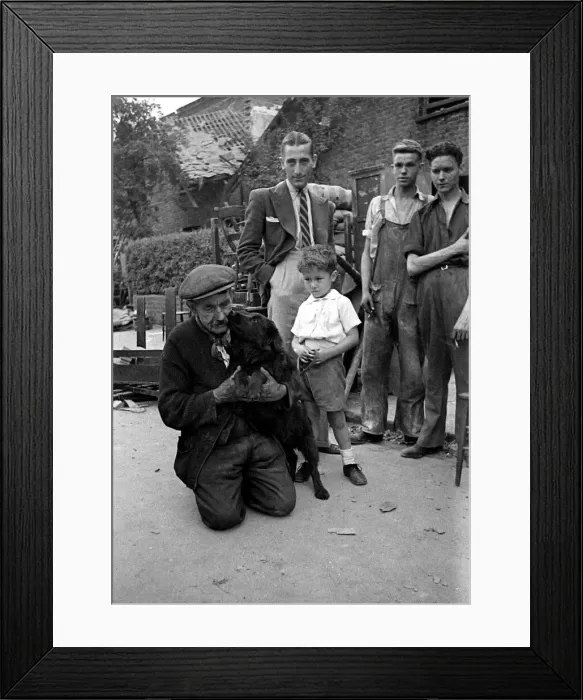 Framed Print : A old man holds his dog as it licks his face watched by a young boy Framed Print : A old man holds his dog as it licks his face watched by a young boy