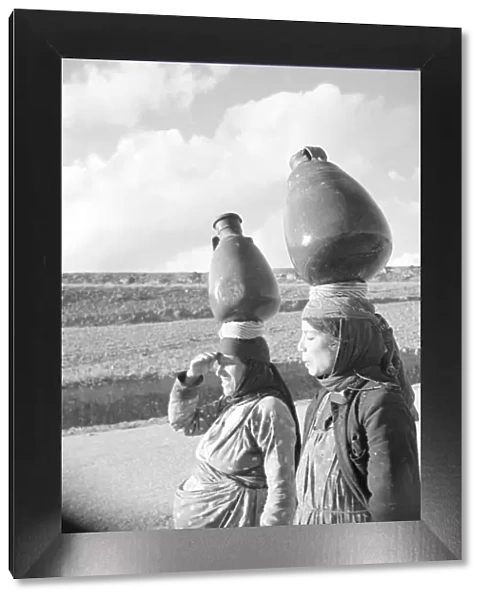 Two Arab women carrying water jars on their head on the Jerusalem road in Palestine