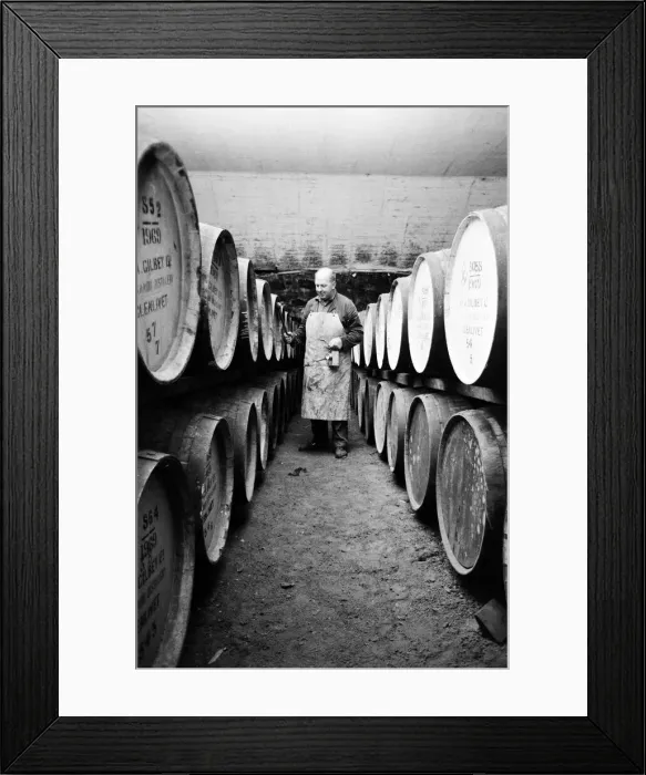 Framed Print : An employee of the Knockando Whisky Distillery checks the casks in the bonded warehouse