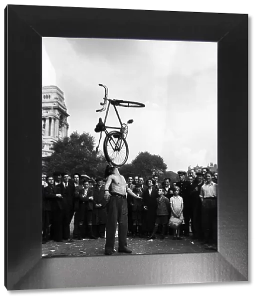A street entertainer at Tower Hill, London balancing a bicycle using his mouth watched by
