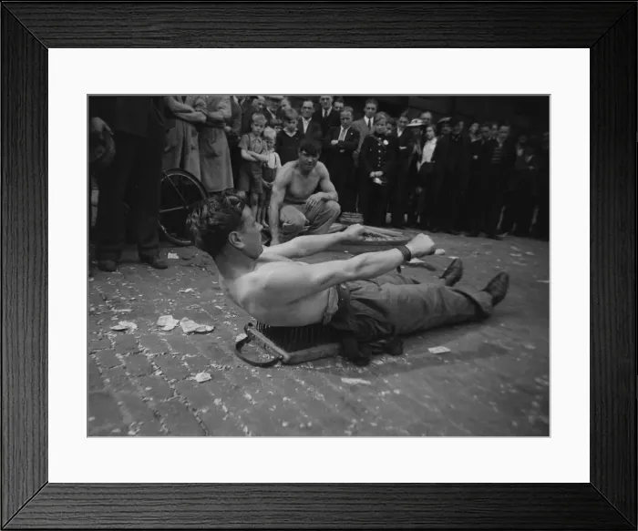 Framed Print : A street entertainer at Tower Hill, London lying on a board of nails watched by a crowd