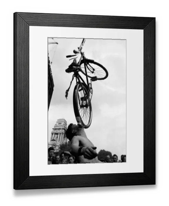 Framed Print : A street entertainer at Tower Hill, London balancing a bicycle using his mouth watched by Framed Print : A street entertainer at Tower Hill, London balancing a bicycle using his mouth watched by