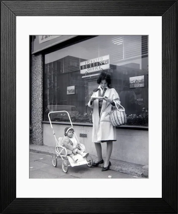 Framed Print : A woman punter studies the form guide outside A E Fane and Co betting shop in islington Framed Print : A woman punter studies the form guide outside A E Fane and Co betting shop in islington