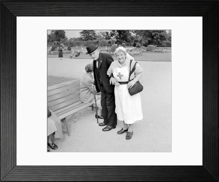 Framed Print : A Red Cross nurse helps and elderly gentleman to a bench during a day trip to Trentham Framed Print : A Red Cross nurse helps and elderly gentleman to a bench during a day trip to Trentham