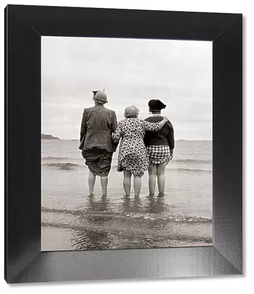 Three women look out to sea watching a ship disappear over the horizon clutching the hems
