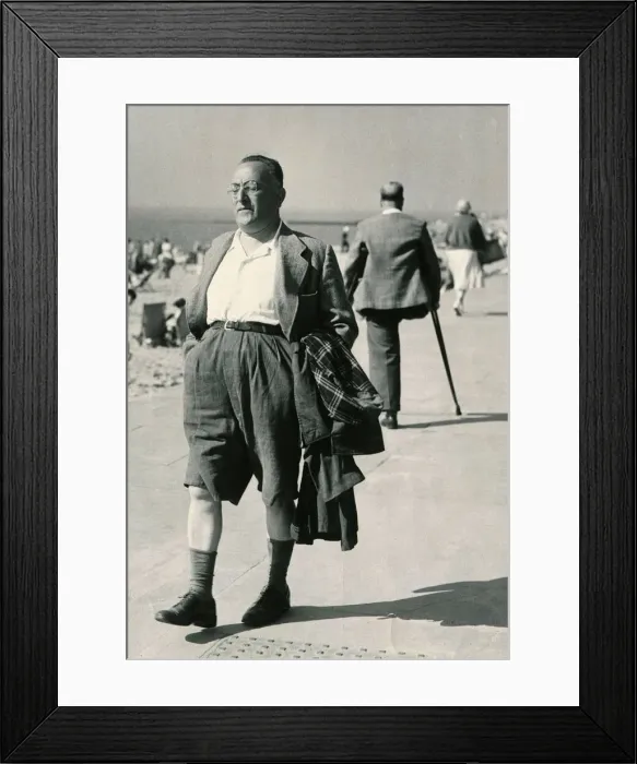 Framed Print : A holidaymaker with his raincoat under his arm strolls along the seafront at Clacton