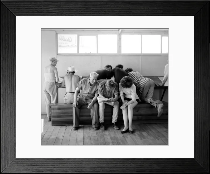 Framed Print : Holidaymakers study the form guide at a betting shop in the form of a wooden chalet