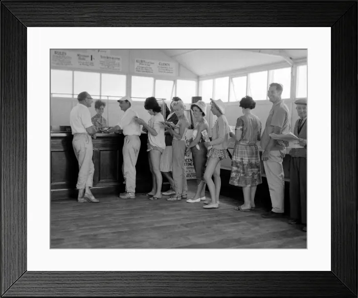 Framed Print : Holidaymakers line up to make a bet at a betting shop in the form of a wooden chalet Framed Print : Holidaymakers line up to make a bet at a betting shop in the form of a wooden chalet