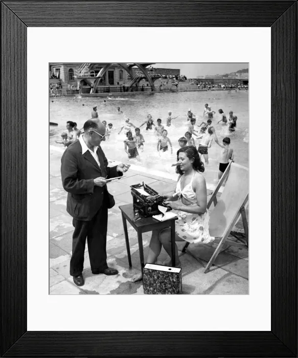 Framed Print : Woman typist working in the sun beside a swimming pool filled with children having fun