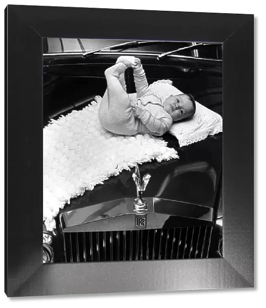 A baby girl lying on a mat on the bonnet of a Rolls poyce Silver Cloud car November