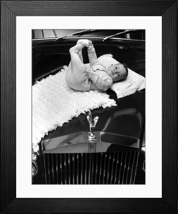 Framed Print : A baby girl lying on a mat on the bonnet of a Rolls poyce Silver Cloud car November
